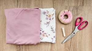 materialien: rosa und gebluemter stoff, schere, naehgarn und donutkissen für stecknadeln